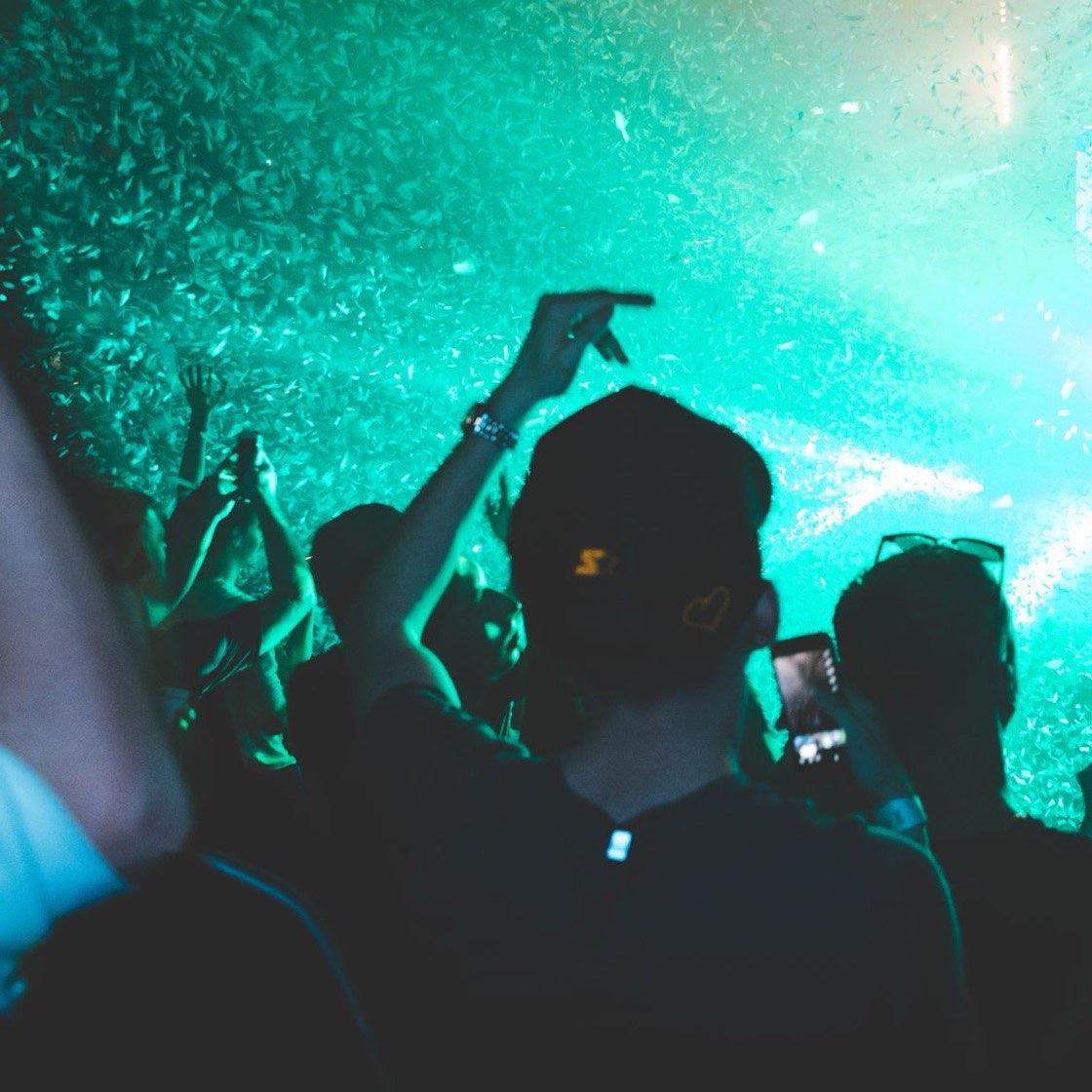 Público con las manos arriba bajo luces verdes en un concierto