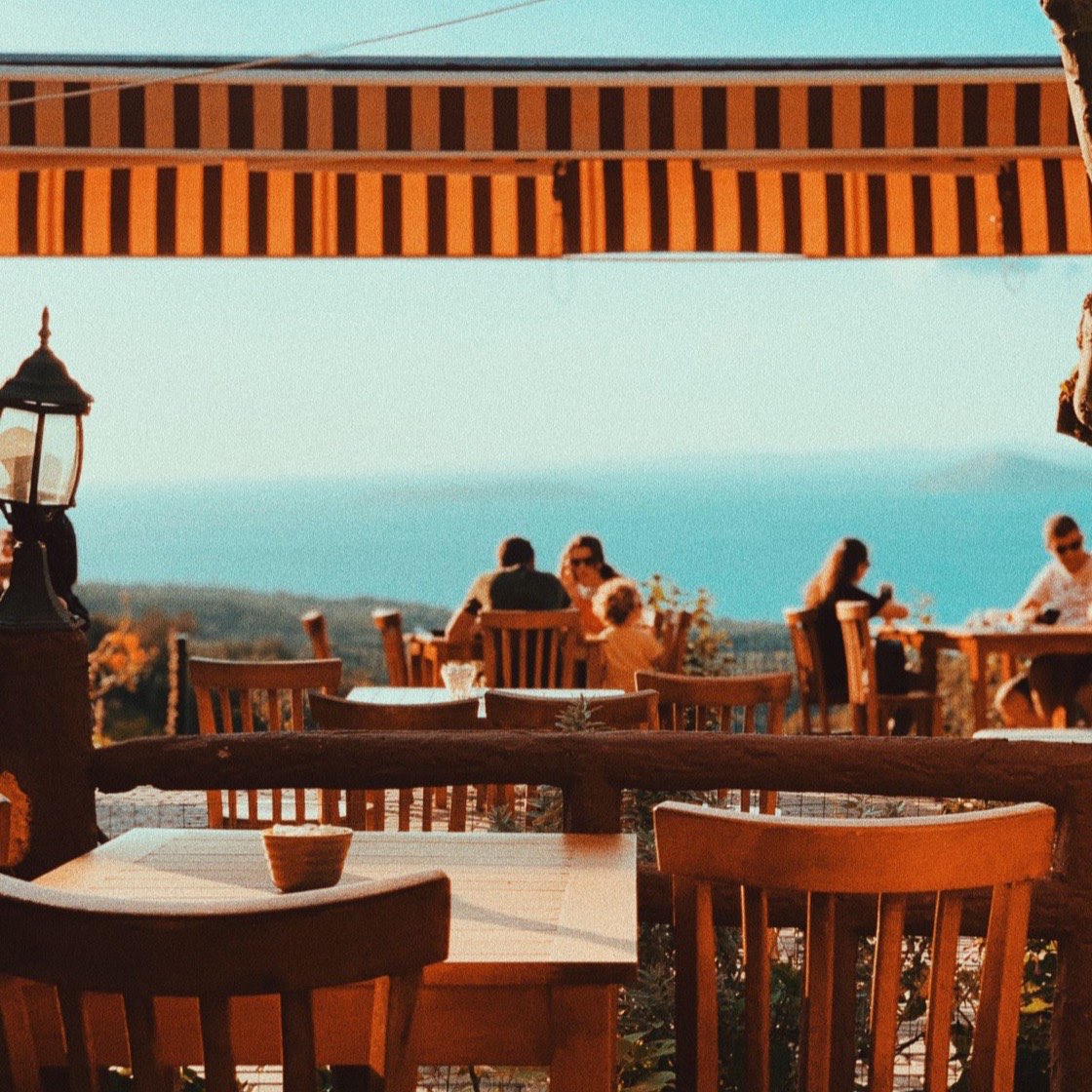 Terraza con mesas y gente cenando al atardecer